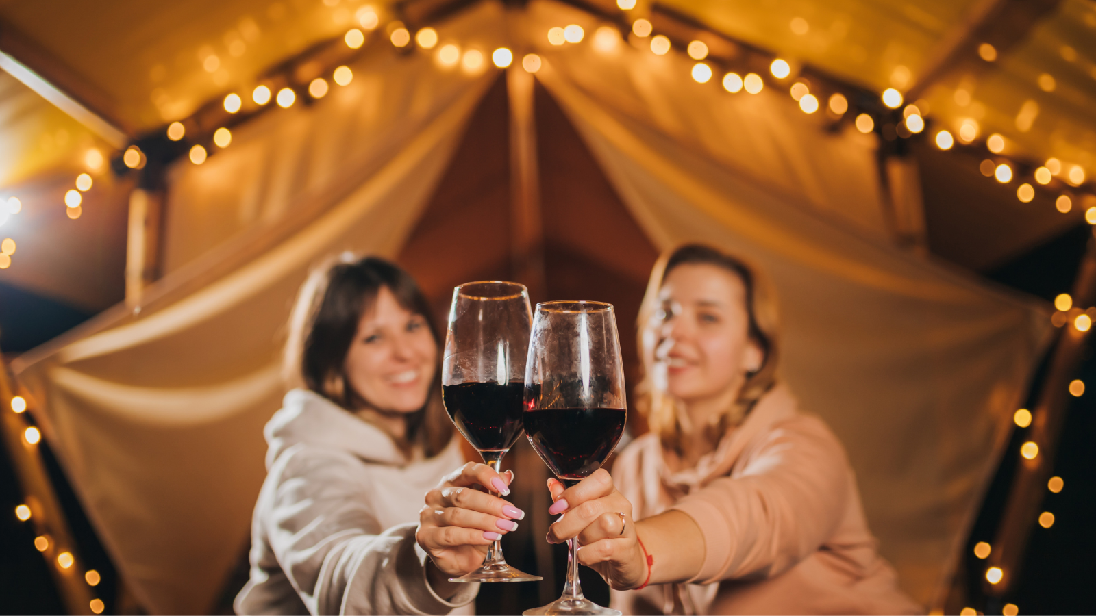 Image of people sat outside a bell tent with a glass of wine